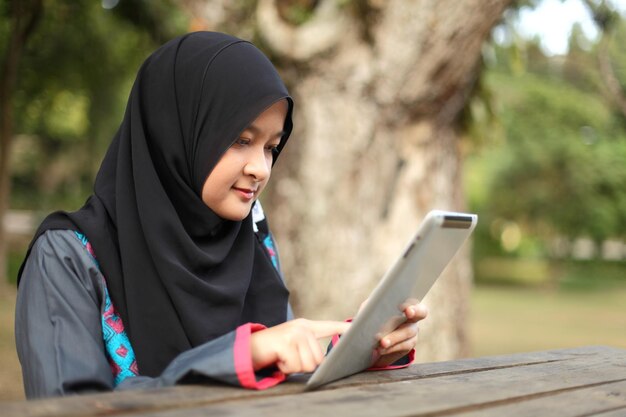 Woman wearing hijab using digital tablet at park