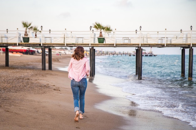 Woman wearing jeans running at sunet on the beach sand