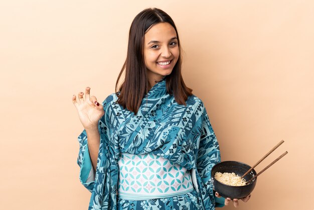 Foto kimono da portare della donna e giudicare una ciotola piena di tagliatelle che mostrano segno giusto con le dita