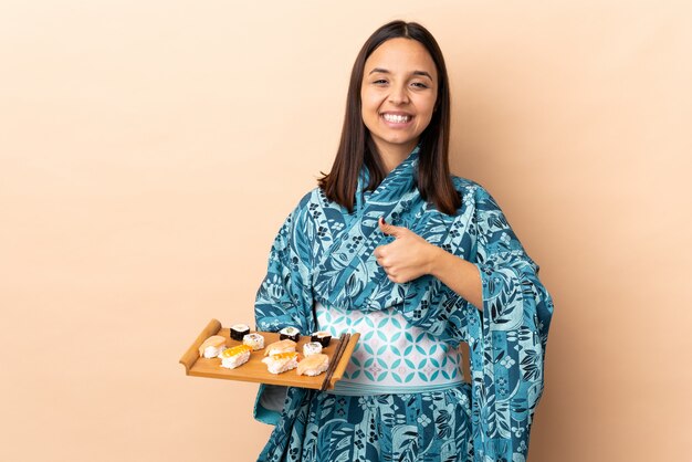 Woman wearing kimono and holding sushi over wall giving a thumbs up gesture