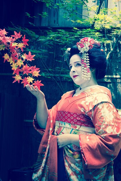 Foto donna in kimono in piedi accanto alle foglie