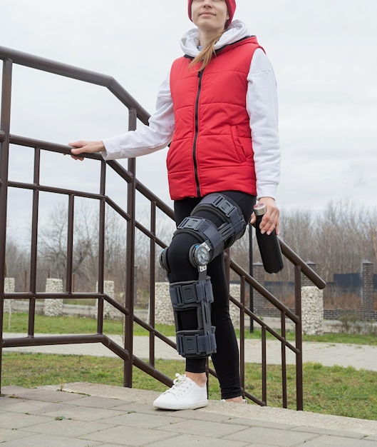 Woman wearing knee brace or orthosis after leg surgery walking in the park