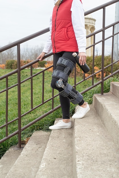 Woman wearing knee brace or orthosis after leg surgery walking in the park