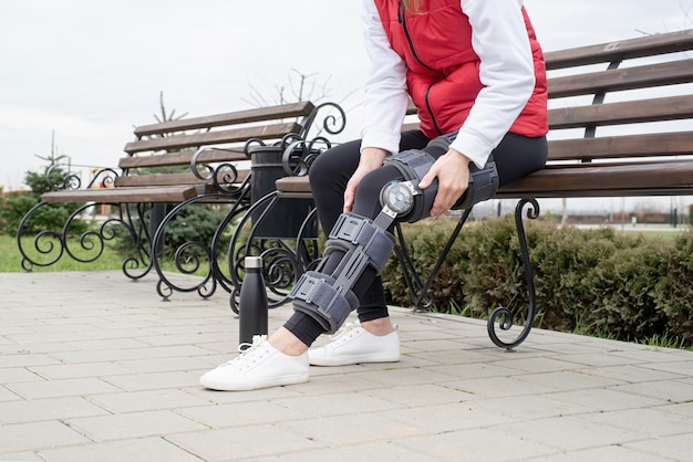 Woman wearing knee brace or orthosis after leg surgery walking\
in the park