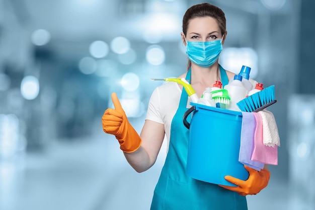 Photo a woman wearing a mask and gloves holds a bucket of cleaning products and a blue bucket with a thumb up.