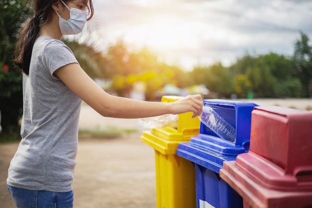 公園のゴミ箱にボトルのプラスチックごみを持っているマスクの手を着ている女性