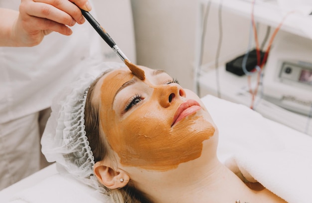 Photo woman wearing a mask on her face in a beauty spa the beautician applies a clay mask to the girls face