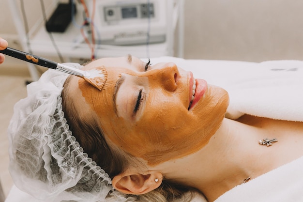 Woman wearing a mask on her face in a beauty spa the beautician applies a clay mask to the girls face