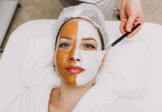 Photo woman wearing a mask on her face in a beauty spa the beautician applies a clay mask to the girls face