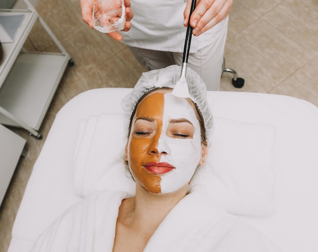 Woman wearing a mask on her face in a beauty spa the beautician applies a clay mask to the girls face