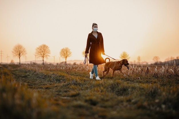 La donna che indossa una maschera cammina da sola con un cane all'aperto a causa della quarantena della corona