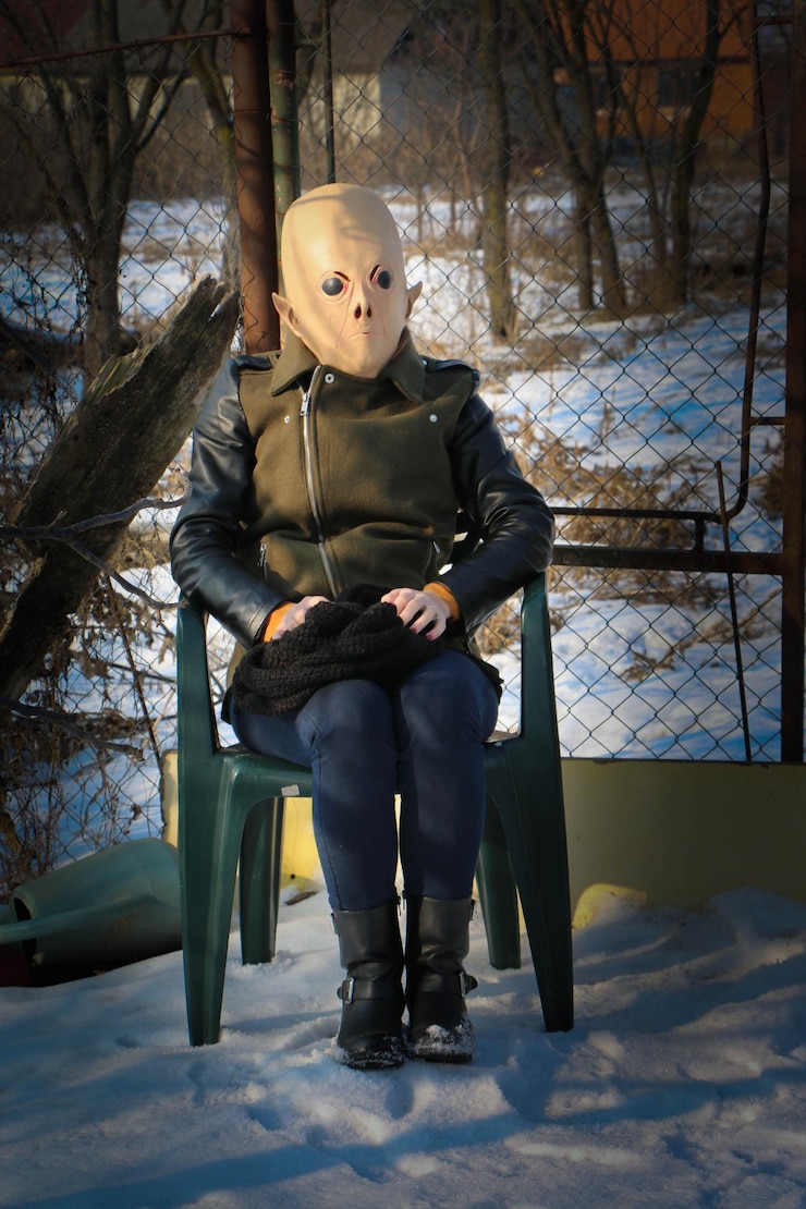 Photo woman wearing mask sitting on chair against fence during winter