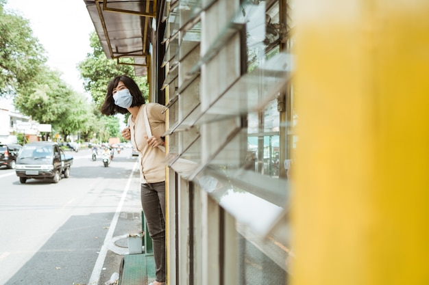 마스크를 쓰고 여자는 버스 정류장에서 버스를 기다리고 서