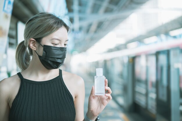 Woman wearing mask and using alcohol gel sanitizer to disinfect Covid-19 virus in metro train station