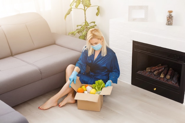 woman wearing medical face mask Disassembles food bags at home in the kitchen. quarantine. health concept. Corona Virus. order of products online. Delivering products to home