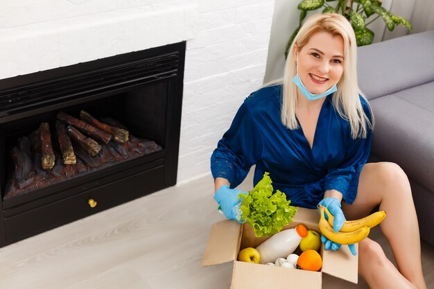 женщина в медицинской маске разбирает пакеты с едой дома на кухне. карантин. концепция здоровья. Корона вирус. заказ товаров онлайн. Доставка продуктов на дом