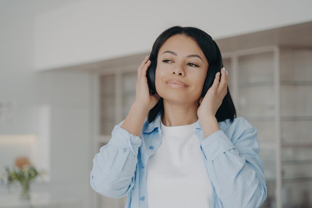 写真 現代のワイヤレスヘッドホンを身に着けている女性は、家で休んでいる音楽ポッドキャストオーディオブックを聴きます