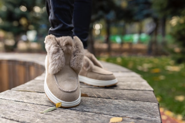 A woman wearing a pair of fur boots stands on a wooden bench in a park.