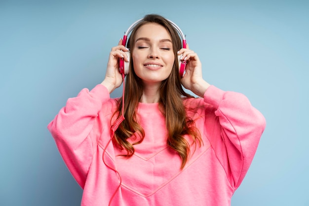 woman wearing pink sweatshirt listening to music in headphones dancing isolated on background