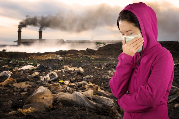 Photo woman wearing pollution mask while standing against factory during sunset