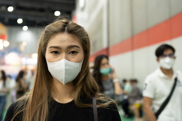 写真 展示会に立ち、ウイルス感染で混雑する保護マスクを身に着けている女性