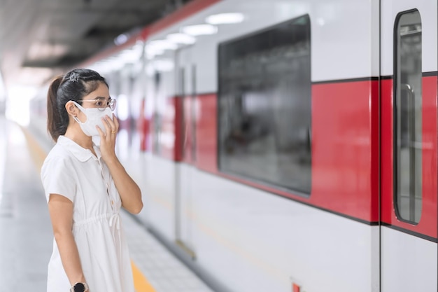 보호용 안면 마스크를 쓴 여성은 기차를 기다리는 동안 코로나바이러스 굴절을 예방합니다. 대중 교통. covid-19 전염병에서 사회적 거리, 새로운 정상 및 안전