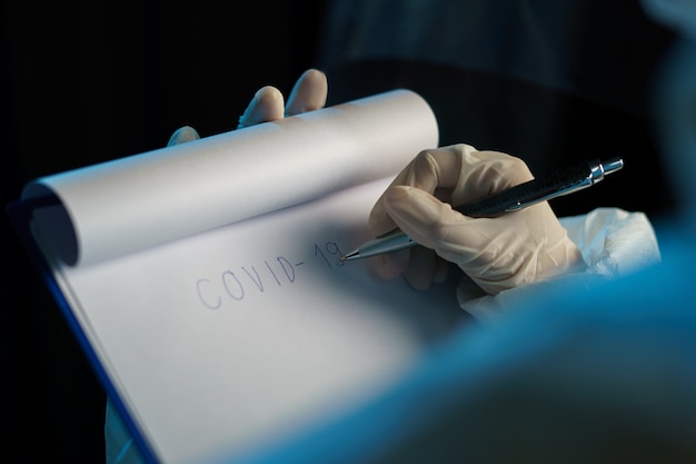 Woman wearing protective hazmat suit and writing virus infected patient's laboratory report.