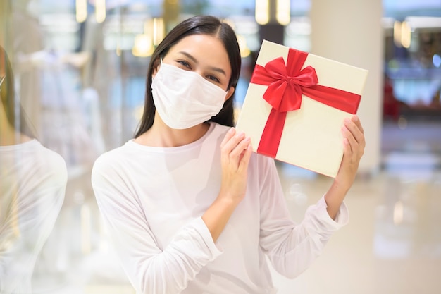 Una donna che indossa una maschera protettiva in possesso di una confezione regalo in un centro commerciale, shopping sotto la pandemia covid-19
