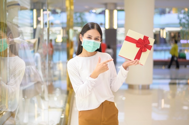 Женщина в защитной маске держит подарочную коробку в торговом центре
