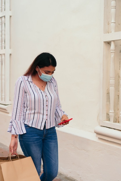 Женщина в защитной маске смотрит на свой мобильный телефон на улице в городе