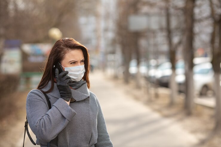 Photo woman wearing protective medical mask outdoors, close up. woman holding a phone. concept self-care