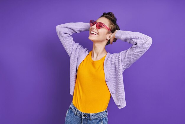 보라색 스웨터와 빨간 안경을 입은 여성이 사진을 찍기 위해 포즈를 취하고 있습니다.