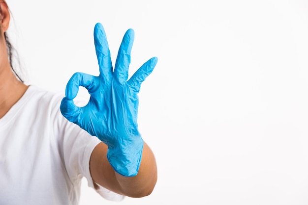 Foto donna che indossa e mette la mano al guanto di lattice di gomma blu per il medico con il segno ok che gesturing