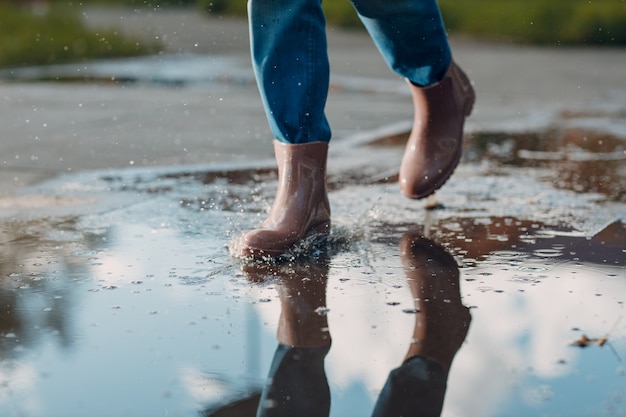 Donna che indossa stivali di gomma da pioggia camminando correndo e saltando nella pozzanghera con spruzzi d'acqua e gocce sotto la pioggia autunnale.