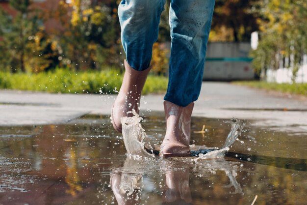 Woman wearing rain rubber boots walking running and jumping into puddle with water splash and drops in autumn rain