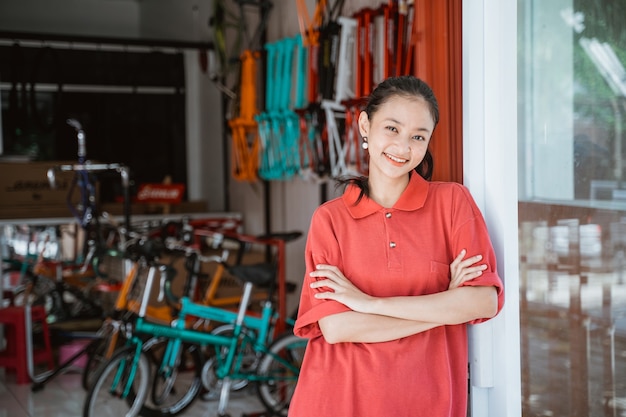 自転車の屋台の前に立っている腕を組んだ赤い襟付きTシャツを着た女性