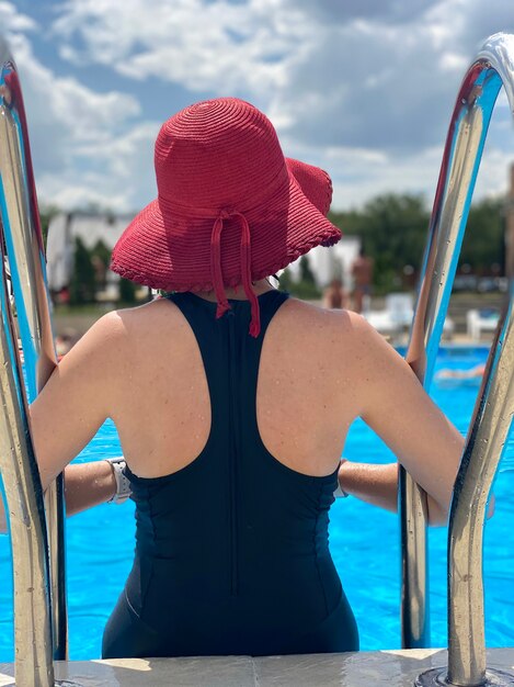 Woman wearing red hat sitting on poolside rear view