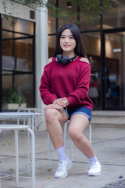 A woman wearing a red sweater and shorts sits on a table outside a cafe