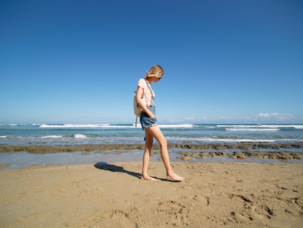 写真 ショートパンツを着た女性が砂浜を歩く。健康的な生活様式。広角ショット。