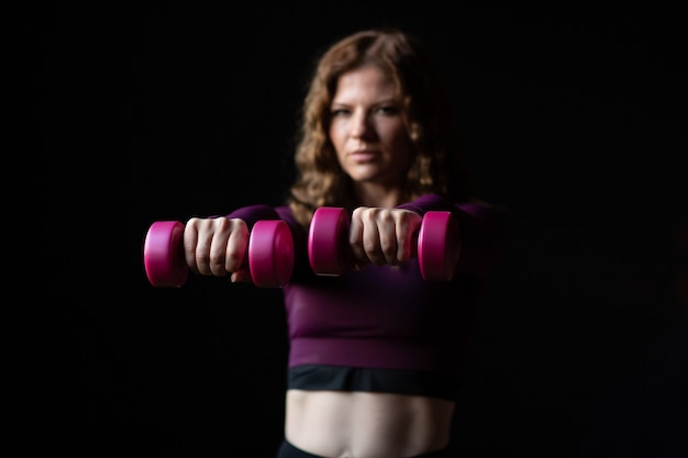 woman wearing sports clothes with pink dumbbells in hands isolated on black background