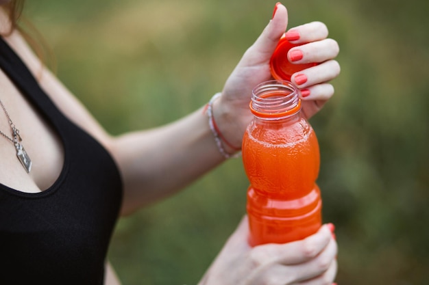 Foto donna che indossa abbigliamento sportivo che si idrata bevendo succo d'arancia vibrante durante l'allenamento sera o mattina nella natura