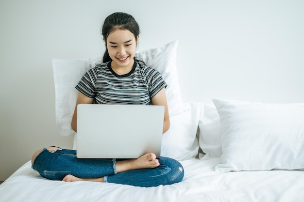 A woman wearing a striped shirt on the bed and playing laptop happily