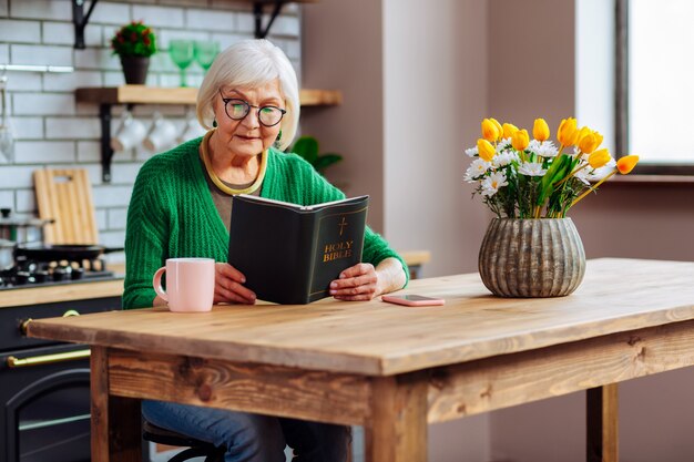 woman wearing stylish green cardigan and glasses holding an open Holy Bible book