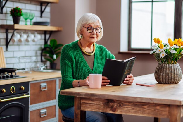 woman wearing stylish green cardigan and glasses holding an open Holy Bible book