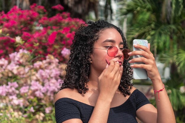 Woman wearing sunglasses doing her make-up outdoors