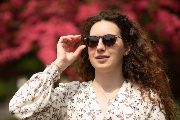 A woman wearing sunglasses stands in front of a bush of azaleas