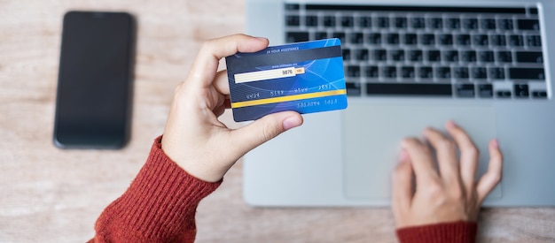 Woman wearing sweater holding credit card and using laptop for online shopping