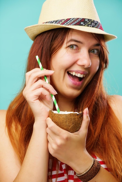 Woman wearing a a swimsuit and straw hat drinks coconaut milk over colorful turquoise background