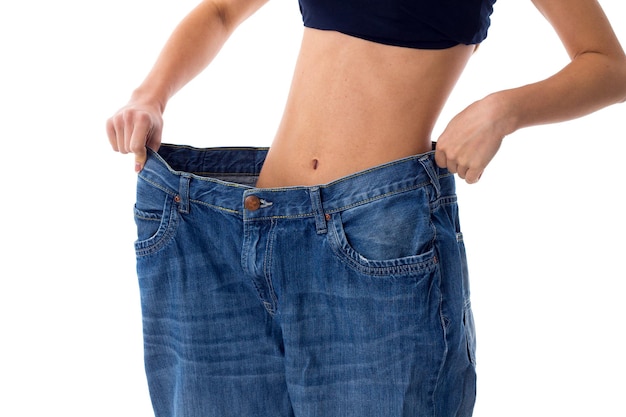 Woman wearing in top and jeans of much bigger size standing on white background in studio