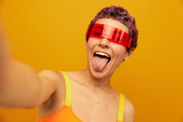 Woman wearing unusual millennial glasses taking selfies in sportswear against an orange studio background free space